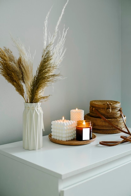 Decoración interior del hogar en colores beige armario con flores secas en jarrón bolsas de ratán y vela