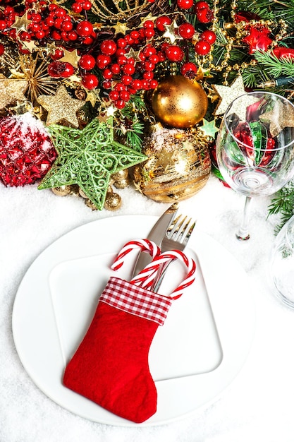 Decoración de lugar de mesa festiva con adornos, guirnaldas doradas, vela roja, ramas de árboles de navidad