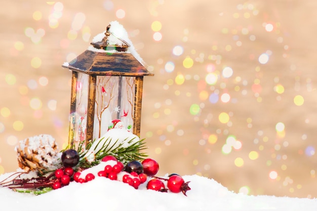 Decoración navideña de año nuevo una postal, una linterna, una rama de abeto con frutos rojos y conos sobre un fondo de luces borrosas.