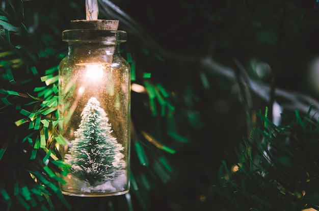 Foto decoración navideña. colgar el pequeño árbol de navidad en un tarro de cristal en ramas de pino guirnalda de árboles de navidad y adornos sobre bokeh abstracto