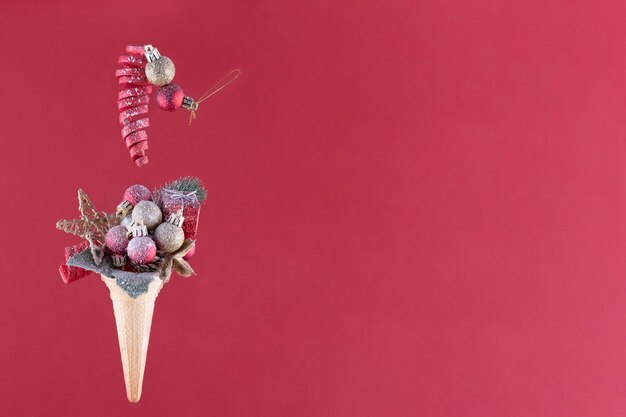 Decoración navideña en cono de helado sobre un fondo rojo detrás del cristal de nieve