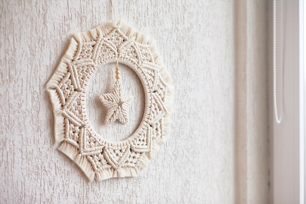 Decoración navideña. Corona de macramé para Navidad y año nuevo en una pared de yeso decorativo blanco. Hilo de algodón natural, cinta de lino. Decoración ecológica para el hogar. Copia espacio