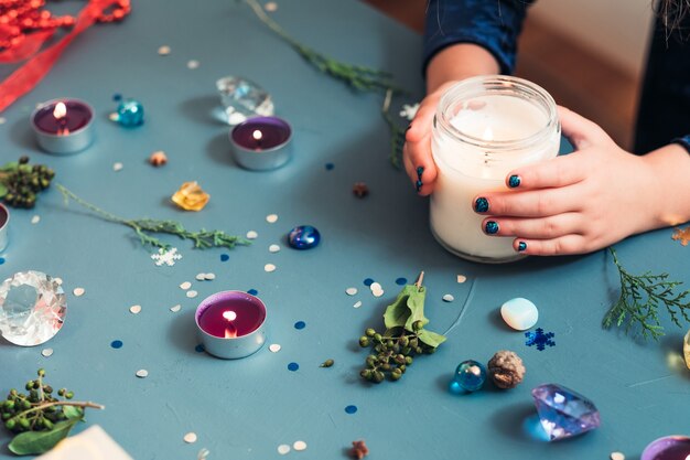 Decoración navideña festiva. manos sosteniendo una vela. adornos de temporada en la pared azul.