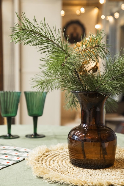 Decoración navideña en la mesa Jarrón con ramas de abeto y vasos con luces en el fondo