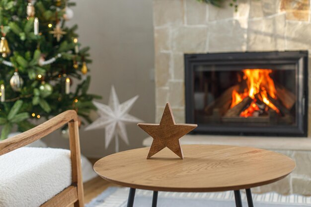 Decoración navideña moderna en la mesa frente a la chimenea ardiente Decoración elegante de estrellas de madera en la sala festiva Nochebuena Tiempo navideño atmosférico