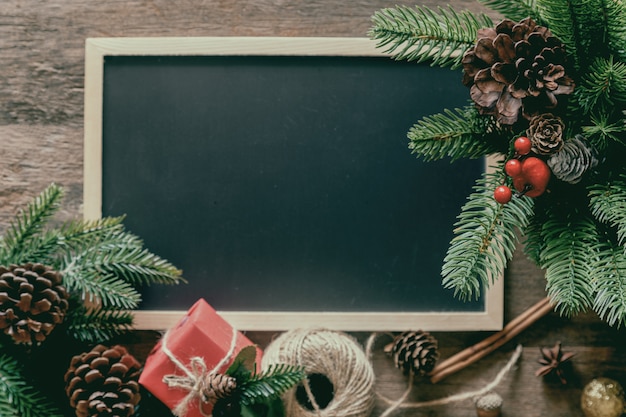 Decoración navideña con pizarra, hojas y conos de pino, caja de regalo y bolas de acebo