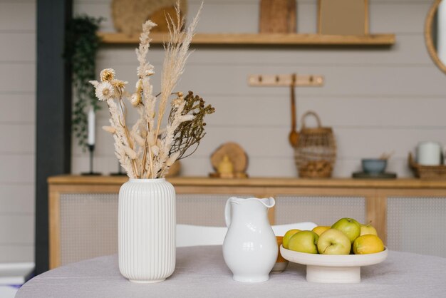 Decoración otoñal de la mesa del comedor Flores secas en un jarrón de cerámica blanca una jarra de leche y manzanas en una bandeja o plato en la cocina escandinava