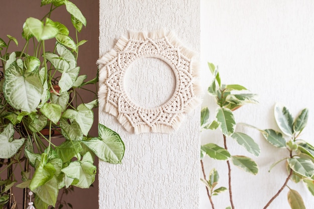 Decoración de pared de mandala de macramé de algodón colgada en la pared blanca con hojas verdes.