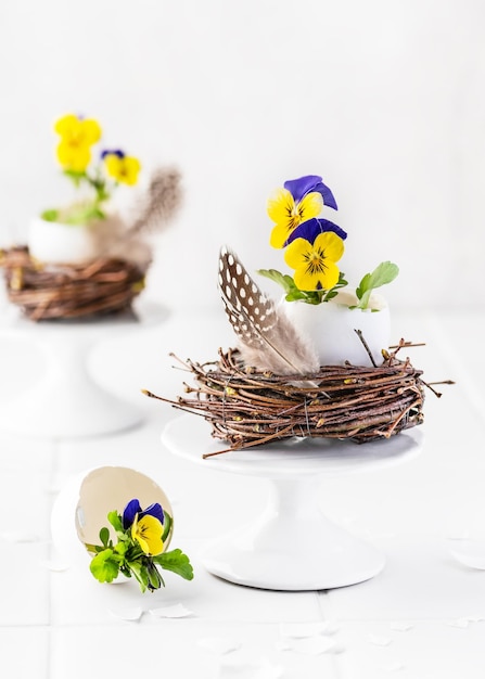 Decoración de pascua hecha a mano con flores de viola moradas y amarillas en jarrón de huevos y nido