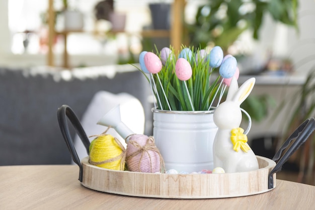 Decoración de pascua de huevos coloridos hierba fresca en una regadera conejito de pascua en una bandeja en la mesa redonda en un estilo rústico Interior festivo de una casa de campo