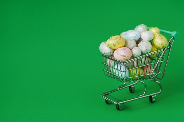 Decoración de Pascua. Huevos de Pascua en carrito de la compra pequeño en mesa verde.