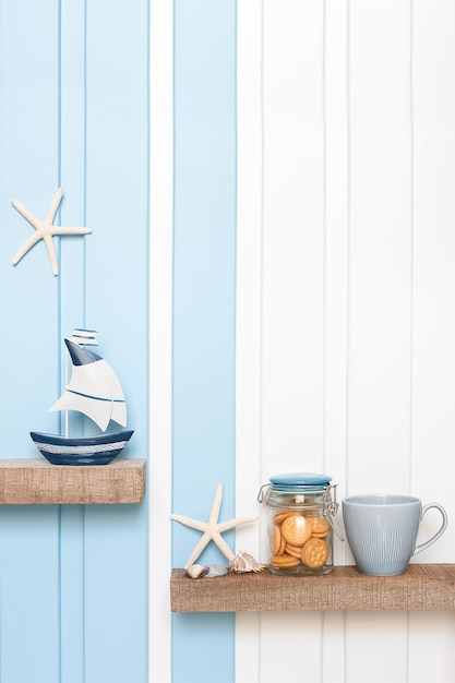 Foto decoración de verano de mar velero estrella de mar concha de café taza de galleta en el estante sobre pared blanca azul