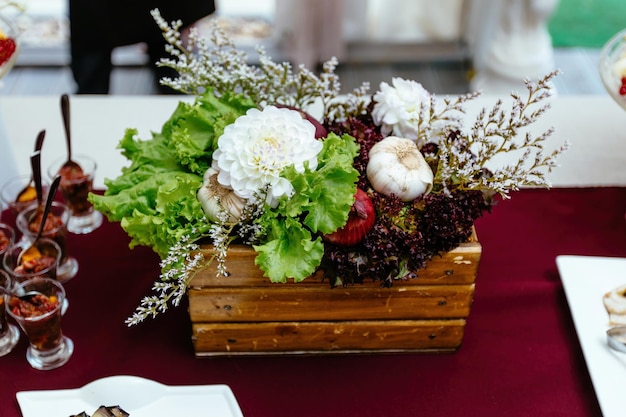 Decoración de verduras y frutas naturales sobre una mesa colocada en una caja de madera y decorada con flores.