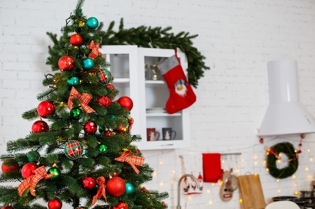 Decoraciones de Año Nuevo en la cocina: un árbol verde decorado con bolas rojas y verdes, decoraciones de Año Nuevo, guirnaldas amarillas. Año nuevo. Decorando la casa para Navidad