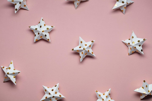 Decoraciones de estrellas blancas y doradas sobre un fondo festivo de temporada rosa pastel