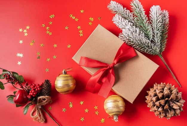 Decoraciones festivas de Navidad y año nuevo con caja de regalo, cono, bolas y rama de árbol de año nuevo sobre fondo rojo.