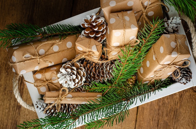 Decoraciones festivas de Navidad con cajas de regalo y conos en caja de madera blanca.