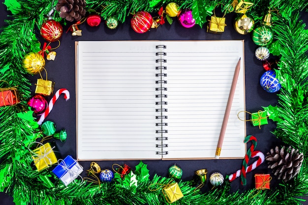 Decoraciones festivas de Navidad con cuaderno vacío y lápiz sobre fondo de papel negro, Ne