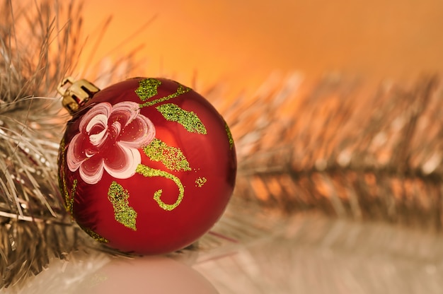 Foto decoraciones de navidad y año nuevo. una bola roja con un patrón y una guirnalda de árbol de navidad se encuentran sobre una mesa. luz de fondo con luz naranja.