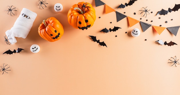 Decorações de Halloween feitas de abóbora, morcegos de papel e aranha preta em fundo laranja pastel. Camada plana, vista superior com espaço de cópia para o texto.