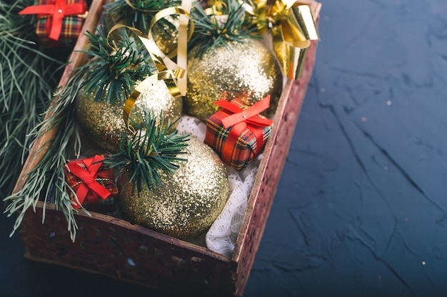 Decorações de Natal, bolas de ouro, em uma caixa de madeira com galhos de pinheiros e pequenos presentes em um fundo cinza escuro