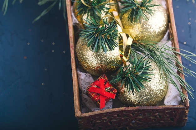 Decorações de natal, bolas de ouro, em uma caixa de madeira com galhos de pinheiros e pequenos presentes em um fundo cinza escuro