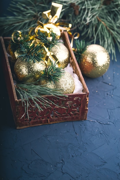 Foto decorações de natal, bolas de ouro, em uma caixa de madeira com galhos de pinheiros em um fundo cinza escuro