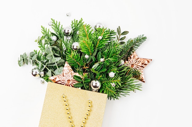 Decorações de Natal brilhantes e ramos de abeto em uma sacola de compras em um fundo branco. Conceito de compras de Natal. Camada plana, vista superior