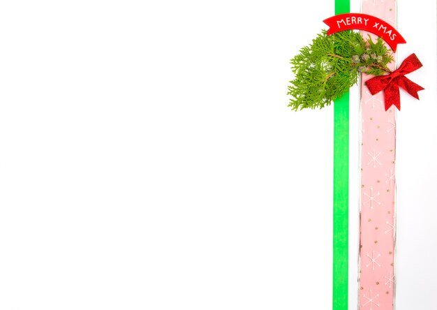 Decorações de Natal colocadas verticalmente ao lado da imagem com copyspace no fundo branco, ramos de pinheiro, fita, arco e sinal de feliz natal