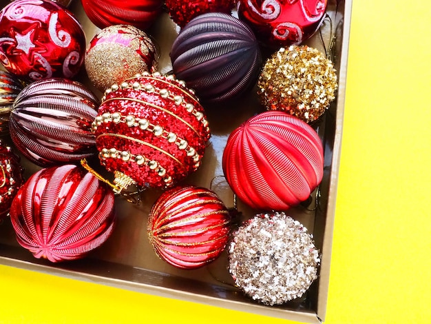 Decorações de Natal em uma caixa em um fundo amarelo Lindas bolas vermelhas e douradas com brilhos