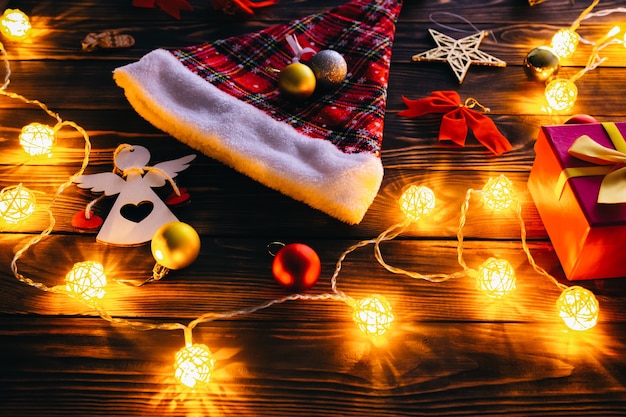 Decorações de Natal na mesa de madeira. Luzes, bugigangas e chapéu de Papai Noel. Clima romântico à noite. Atmosfera acolhedora. Férias plana leigos. Conceito festivo. Ano novo de 2021.