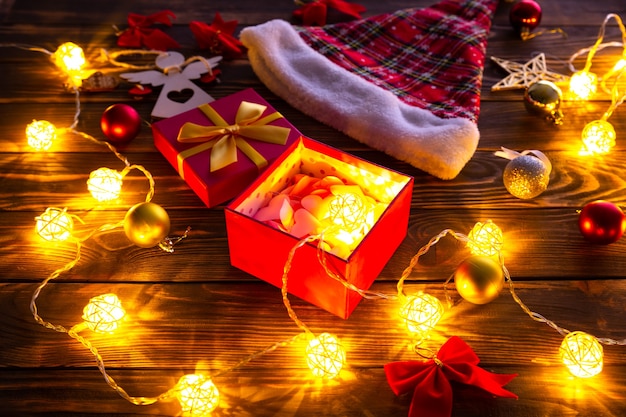 Decorações de Natal na mesa de madeira. Luzes, bugigangas e chapéu de Papai Noel. Clima romântico à noite. Atmosfera acolhedora. Férias plana leigos. Conceito festivo. Ano novo de 2021.