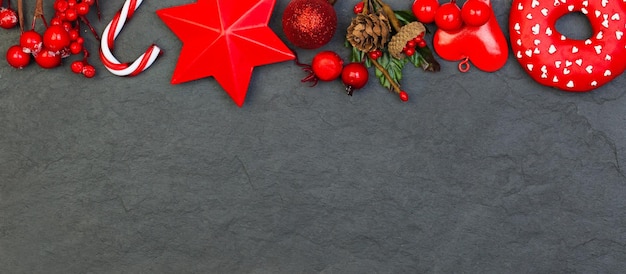 Decorações de Natal vermelhas sobre fundo preto Composição colorida com bagas de azevinho estrelas vermelhas e bugiganga de vidro