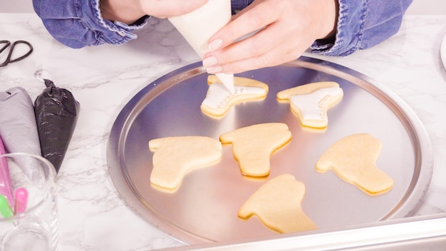 Decorando biscoitos de açúcar em forma de patins de gelo com glacê real de cor branca.