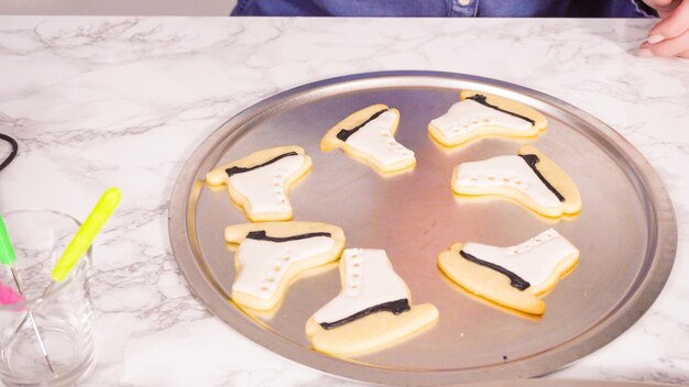 Decorando biscoitos de açúcar em forma de patins de gelo com glacê real de cor preta.