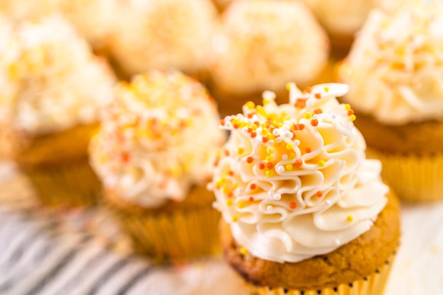 Decorando o cupcake de especiarias de abóbora com creme de manteiga italiano e granulado.