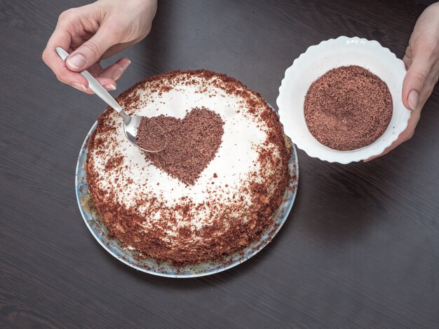 Decorar un pastel para el día de San Valentín. Tarta hecha a mano con glaseado de queso crema y un corazón de chocolate. Dulces para San Valentín