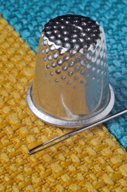 Dedal y aguja de coser sobre tela amarillo-azul. de cerca.