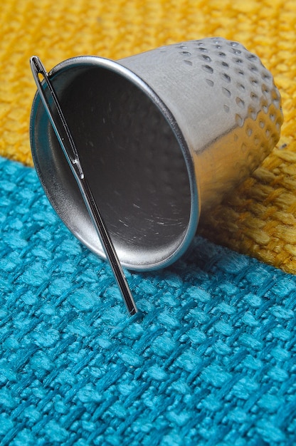 Dedal y aguja de coser sobre tela amarillo-azul. de cerca.