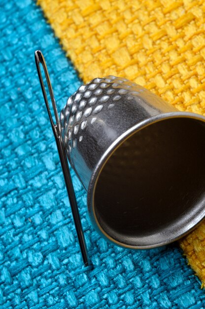 Foto dedal e agulha de costura em tecido amarelo-azulado. fechar-se.