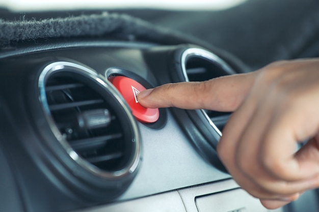 Dedo de mulher, pressionando o botão de emergência no painel do carro em tom de cor vintage