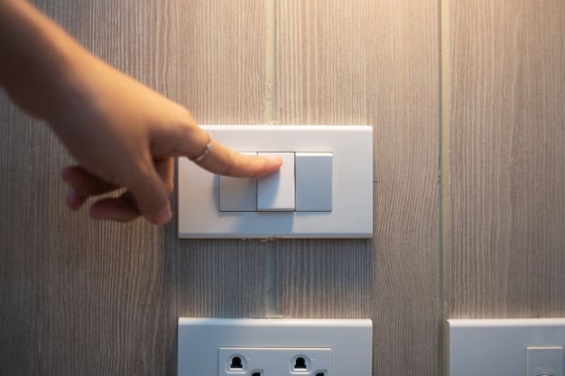 Dedo feminino é ligar ou desligar o interruptor de luz na parede branca em casa. Conceitos de economia de energia, energia, elétrica e estilo de vida.