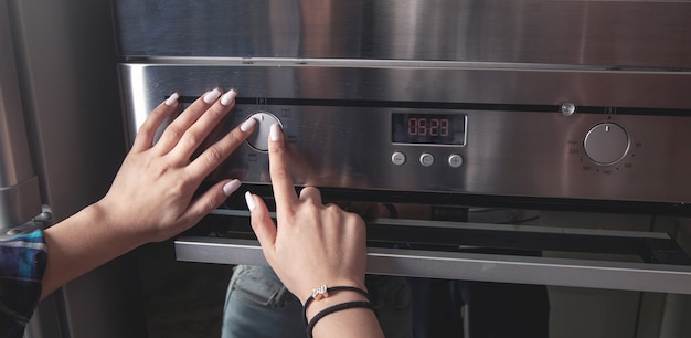 Foto dedo feminino tocando o botão do forno elétrico na cozinha.