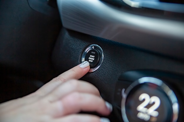 El dedo de la mano del conductor presiona el botón de inicio y parada en un automóvil moderno. de cerca. no cara. Opción sin llave en coche. enfoque selectivo