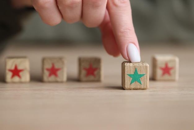 Dedo de mujer toca cubo de madera para niños con estrella verde contra bloques con concepto de estrellas rojas