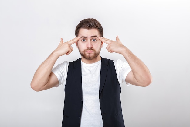 Dedo na têmpora. jovem bonito com barba em uma camisa branca e um colete preto, atirando com o dedo na cabeça.