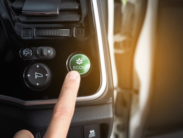 Dedo no botão do modo de economia de energia do carro ecológico com reflexo de luz