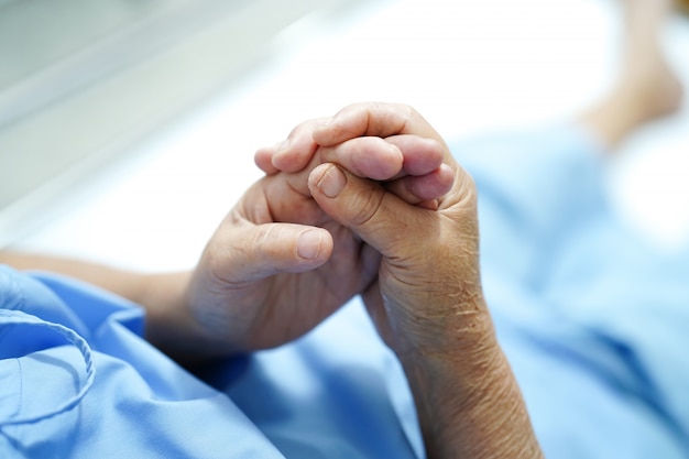 Dedo paciente y mano mayores o mayores asiáticos del dolor de la mujer mayor asiática mientras que se sienta en cama.
