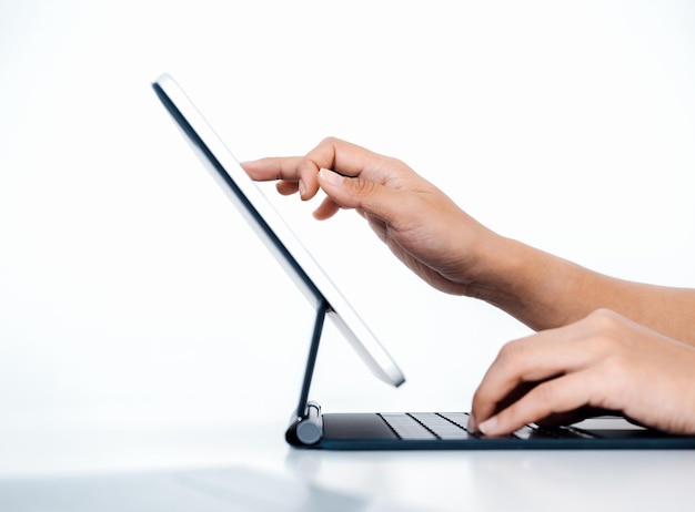El dedo de la persona toca el dibujo en la pantalla de la tableta digital mientras escribe en el teclado de la computadora con otra mano aislada en fondo blanco con vista lateral del espacio de copia Trabajar con tecnología