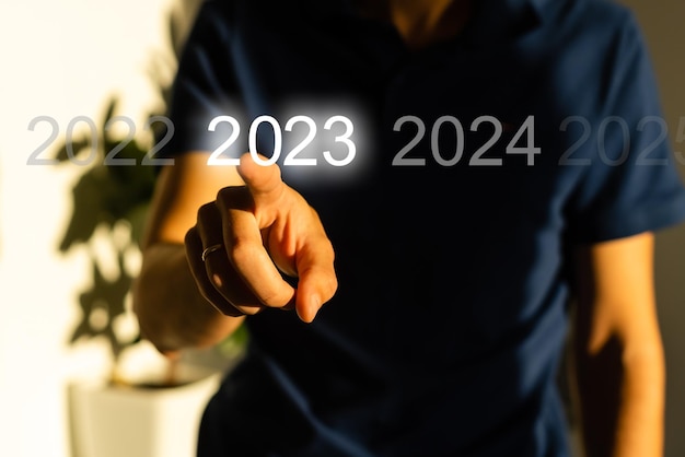 Foto dedo pressionando o botão azul iniciar 2023 na interface virtual em fundo cinza com espaço de cópia para o texto. conceito de ano novo. empresário pressionando 2023 iniciar negócios. início do ano novo 2023